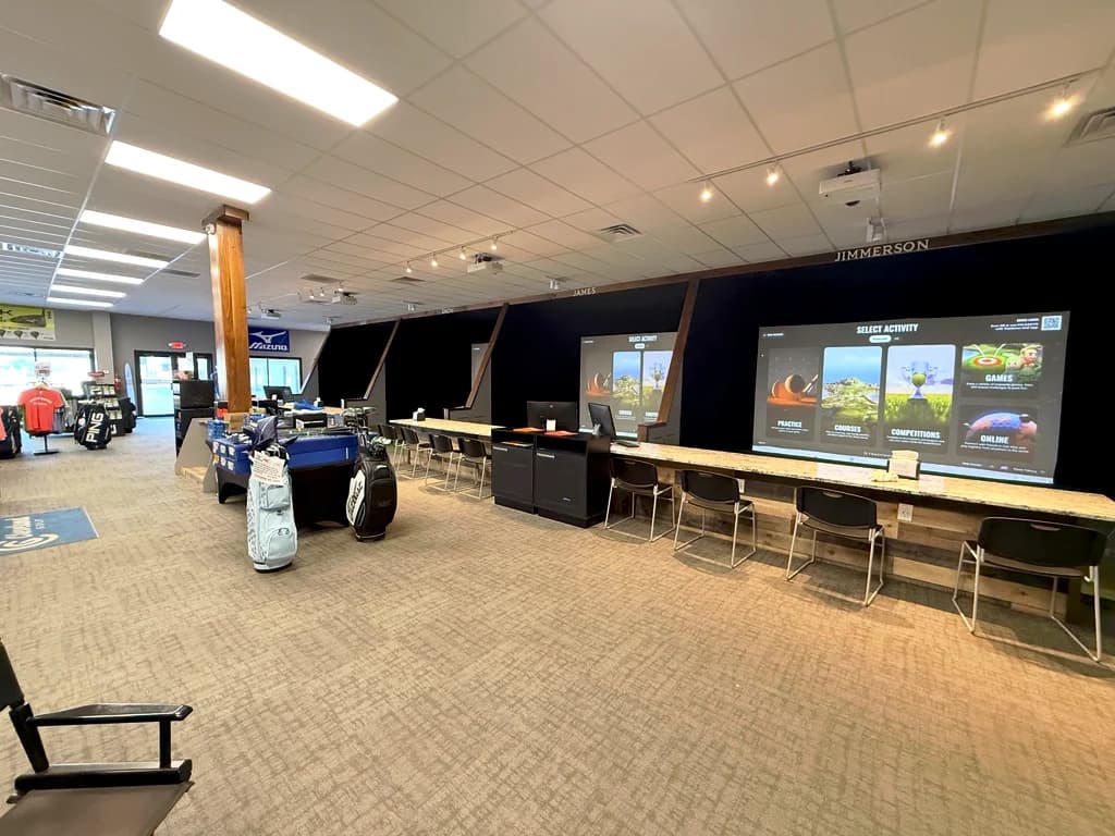 The simulator bays at Tilbury Golf Academy: a row of TrackMan screens with counter seating beside the pro shop