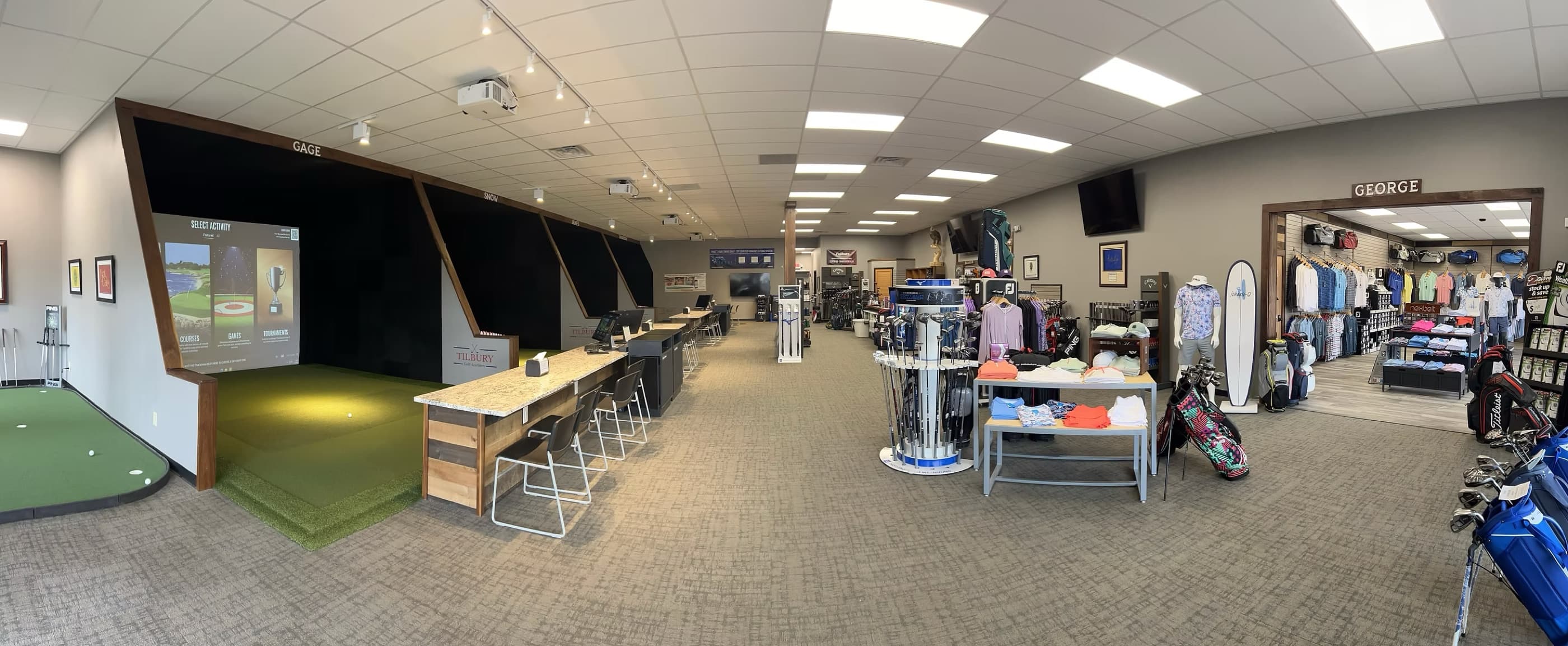 Panoramic view inside Tilbury Golf Academy: TrackMan simulator bays, putting green, and pro shop